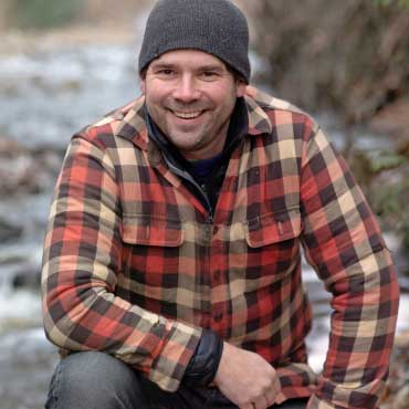 Portrait of Dr. Adam Ford kneeling beside a stream