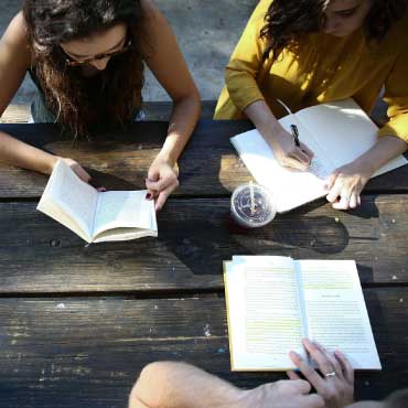 Three people reading books on a bench outdoors