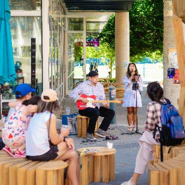 A person playing a guitar and a person singing in front of a group of listeners outside