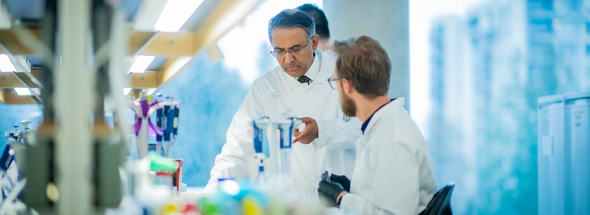 Two people in lab coats interacting with each other and lab equipment