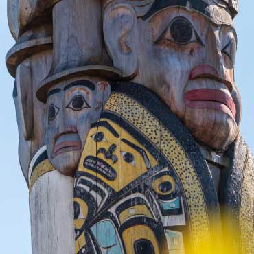 A close-up of a reconciliation pole carved with human faces against a clear sky