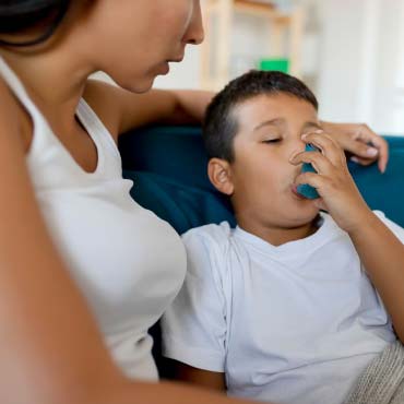 Child using asthma inhaler while sitting beside parent