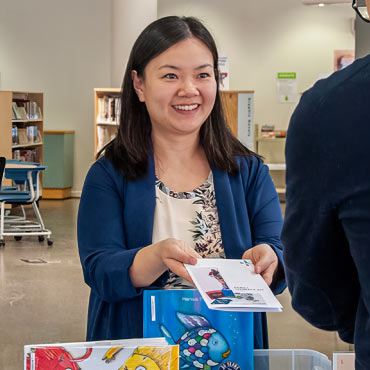 Person smiling and handing a book to a patron.