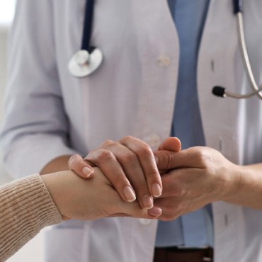 A doctor in white attire with a stethoscope comforts a patient.