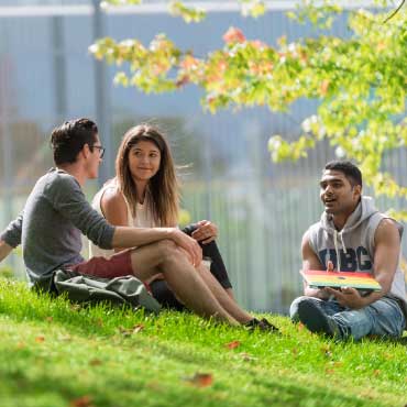 Three students sitting on the grass and talking