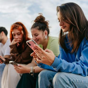 A group of young individuals seated on a bench, each focused on their smartphones, immersed in their digital devices.