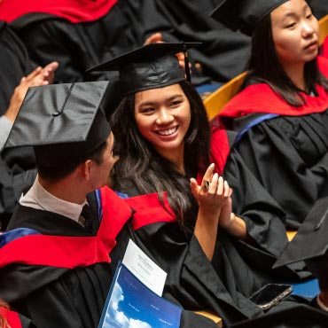 A smiling graduate enthusiastically claps for the audience