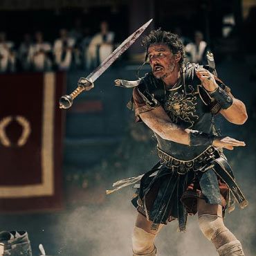 A man in a Roman outfit stands confidently, gripping a sword