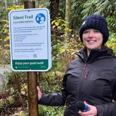 A woman stands beside a sign that reads "Silent Trail"