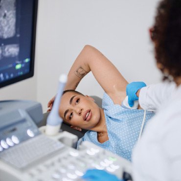 A woman lies comfortably as a technician performs an ultrasound on her arm