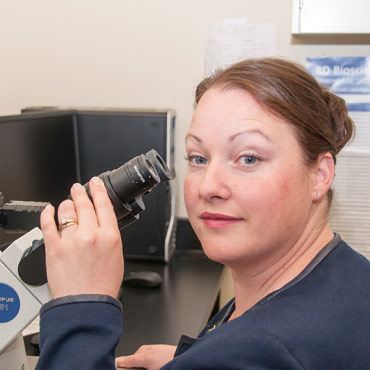 Dr. Deanna Gibson holding microscope in the lab.