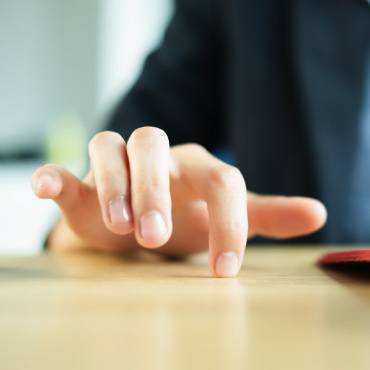 Person's hand fidgeting on table top.