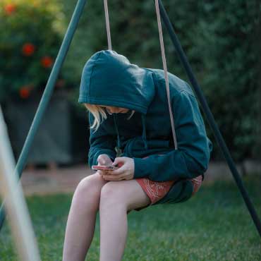 Youth sitting on a swing while using mobile phone